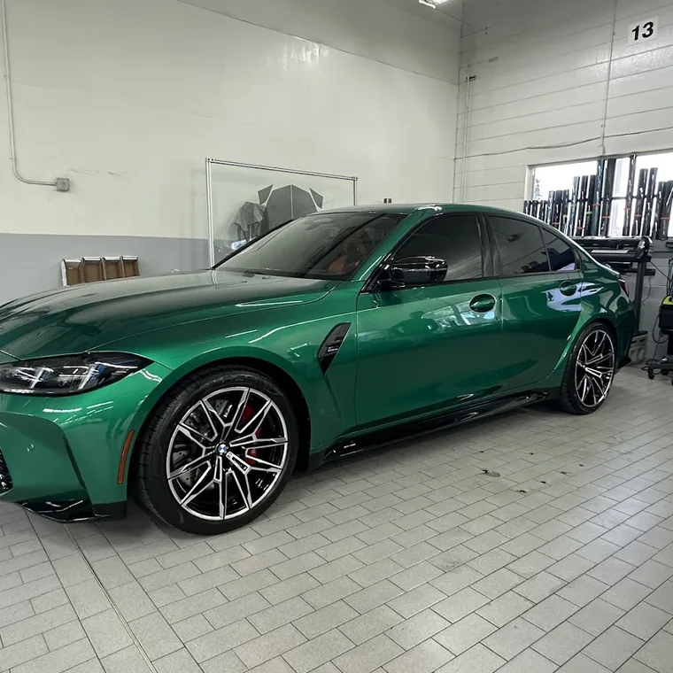 A green BMW M4 with tinted windows in the workshop